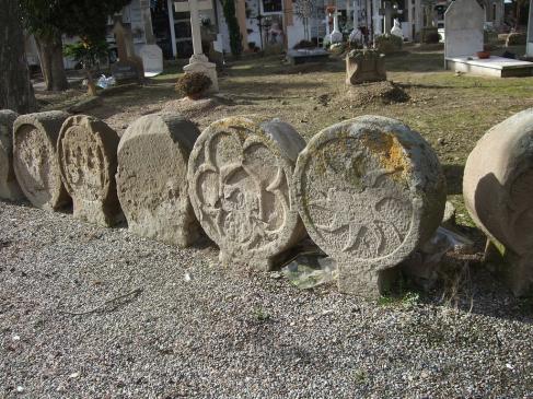 20.8.2007 Fragment de la sèrie de les gairebé 70 esteles funeràries visibles al cementiri de Sanaüja. Tot i estar en una fase de degradació galopant, a l'estar exposades a l'intempèrie, encara predomina la seva més o menys fàcil identificació. En la que veiem en primer terme podem observar una roda solar. El conjunt d'esteles és datable en el periode comprés des del s. XIII al XIX, amb una abundant representació de les èpoques medievals.         Sanaüja. Cementiri -  Jordi Bibià